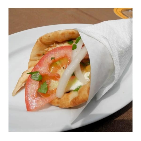 A Zait & Za'atar chicken shawarma with tomatoes, onions, and sauce, wrapped in pita bread.