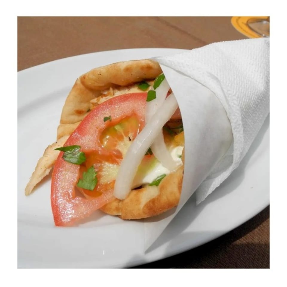 A Zait & Za'atar chicken shawarma with tomatoes, onions, and sauce, wrapped in pita bread.
