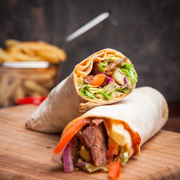 Two Zait & Za'atar shawarmas, filled with meat and vegetables, on a wooden board with fries.