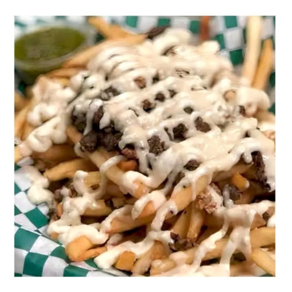 Zait & Za'atar's loaded fries with meat and white sauce, served in a green and white checkered basket.