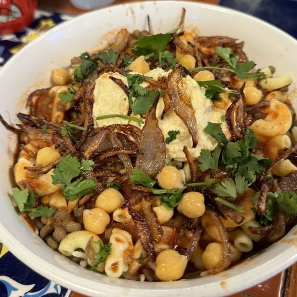 A close-up of a Koshary bowl from Zait & Za'atar, topped with crispy onions, chickpeas, and cilantro.