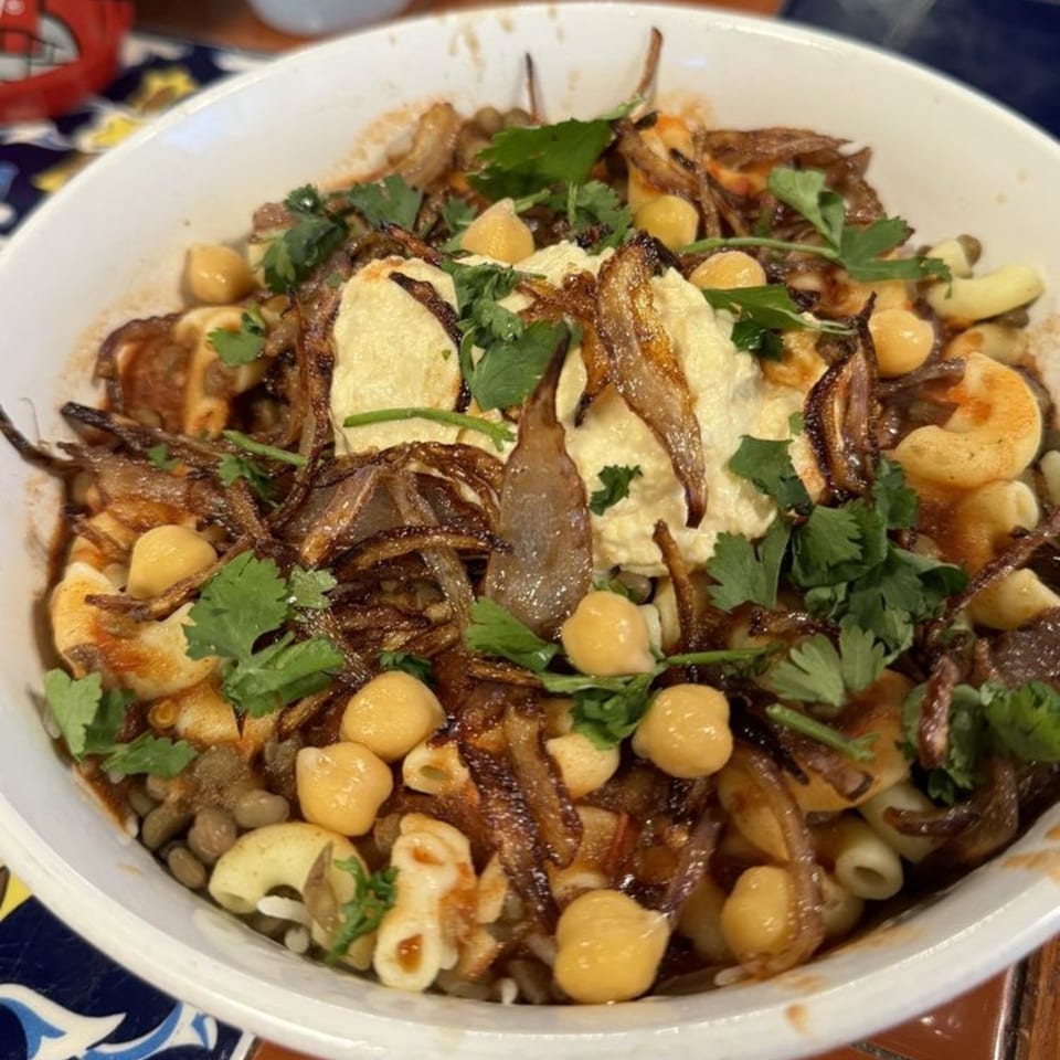A close-up of a Koshary bowl from Zait & Za'atar, topped with crispy onions, chickpeas, and cilantro.