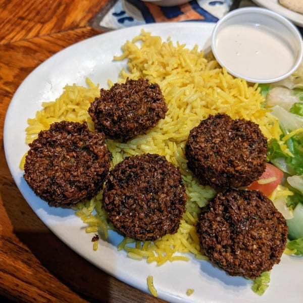 Five falafel patties on a bed of yellow rice with a side salad and white sauce.